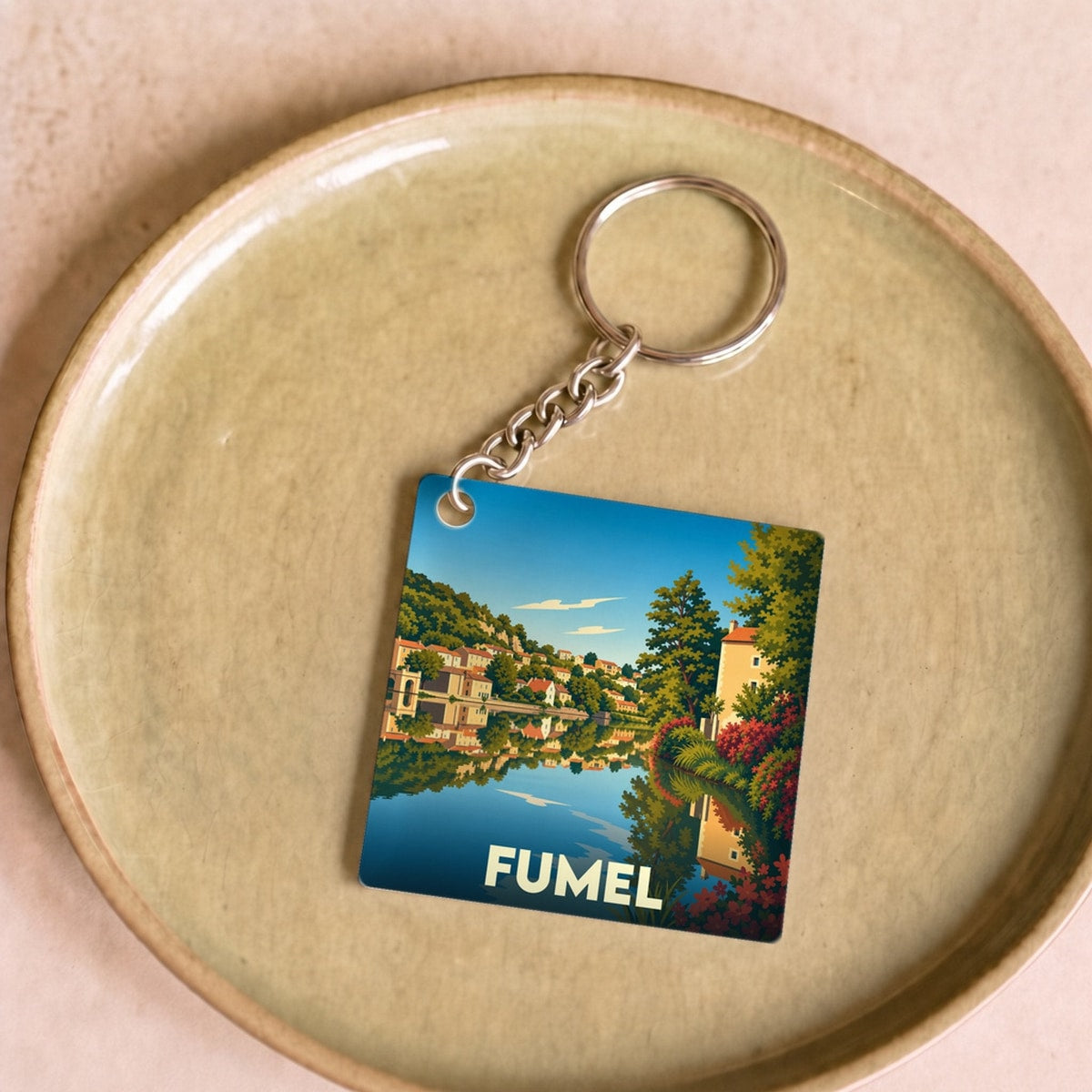 Porte-clés souvenir de la ville de Fumel avec une illustration stylisée et colorée de ses paysages au bord de l'eau.