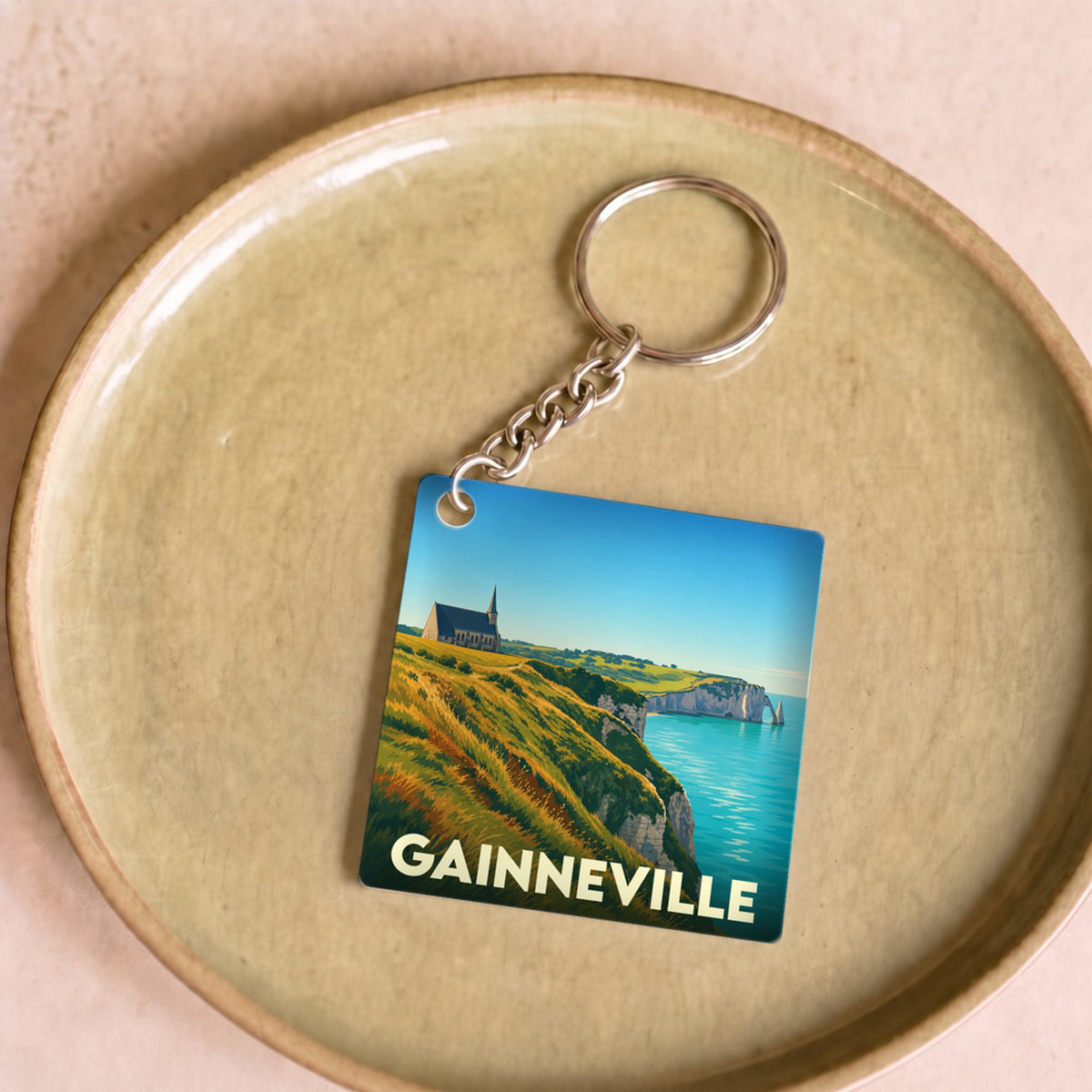 Porte-clés souvenir de la ville de Gainneville avec une illustration stylisée de falaises en bord de mer.