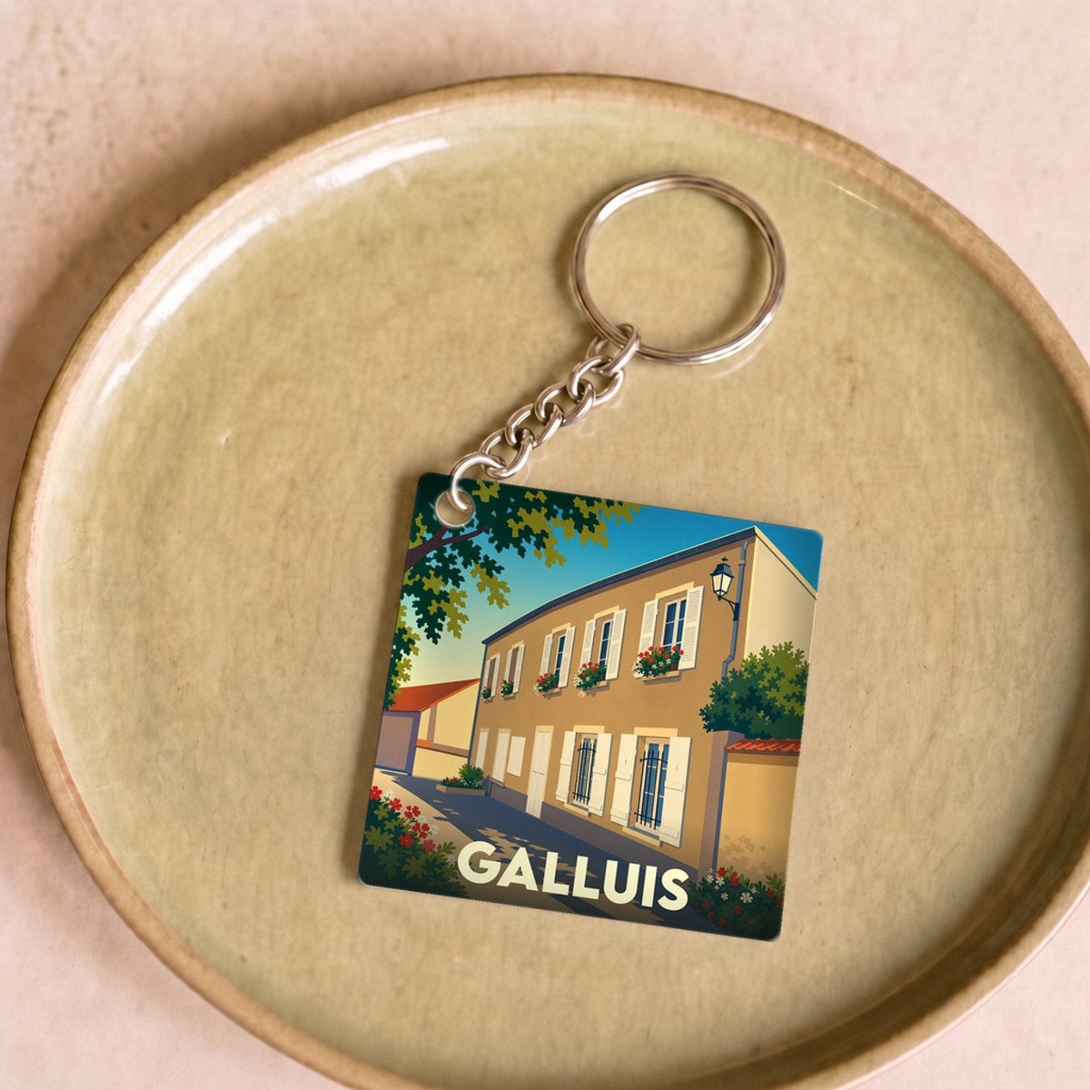 Porte-clés souvenir de la ville de Galluis avec une illustration stylisée d'une rue ensoleillée.