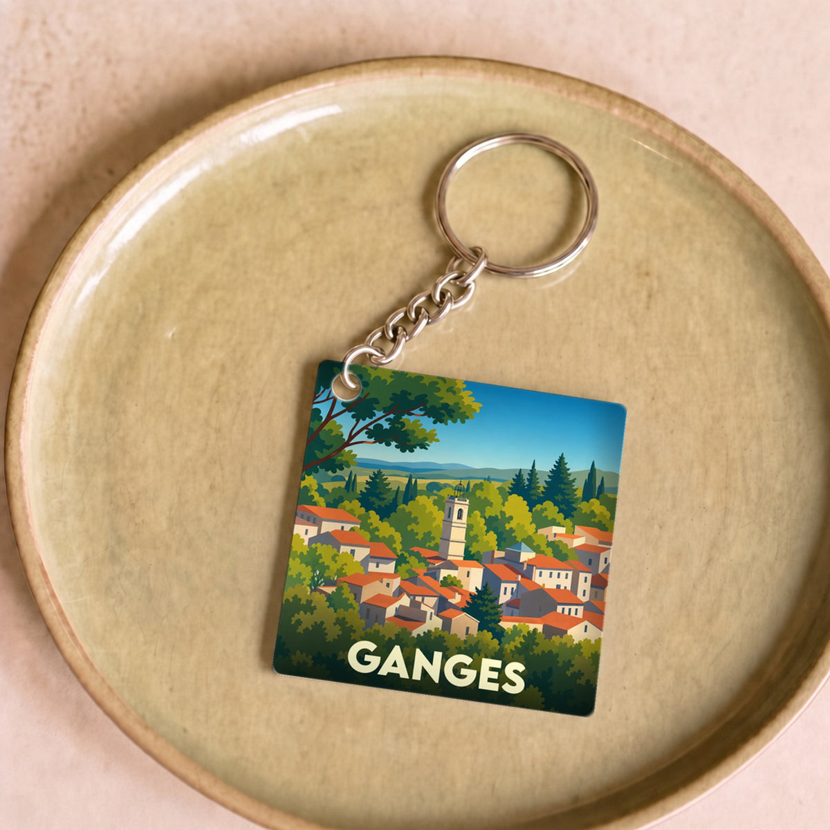 Porte-clés souvenir de la ville de Ganges avec une illustration stylisée d'un village pittoresque.