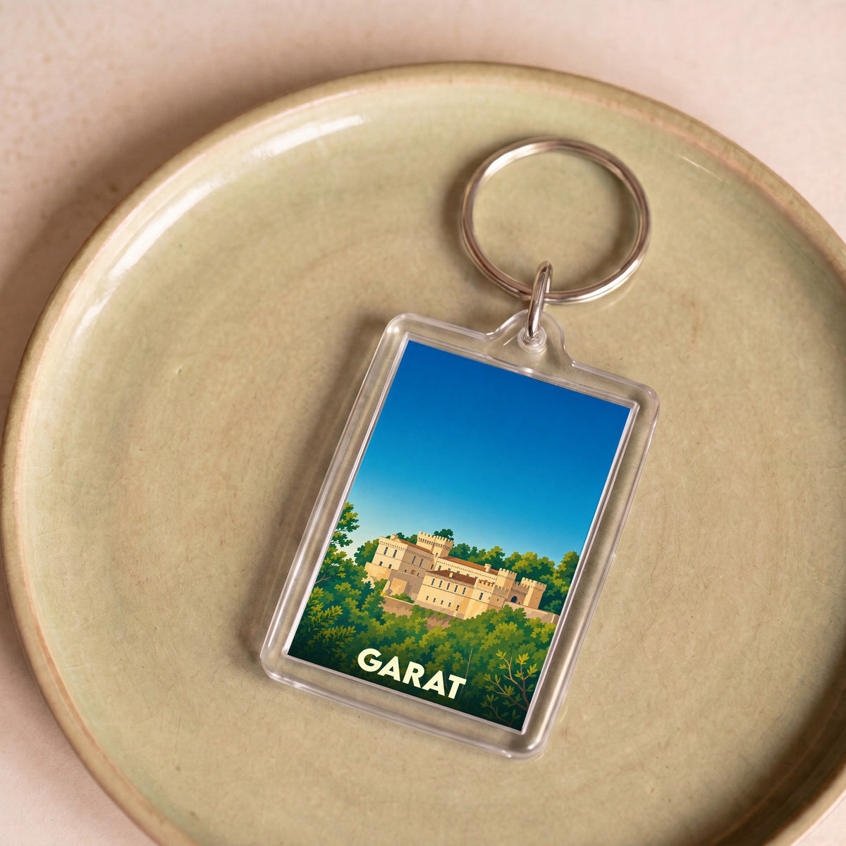 Porte-clés souvenir de la ville de Garat illustré d'un château entouré de verdure sous un ciel bleu.