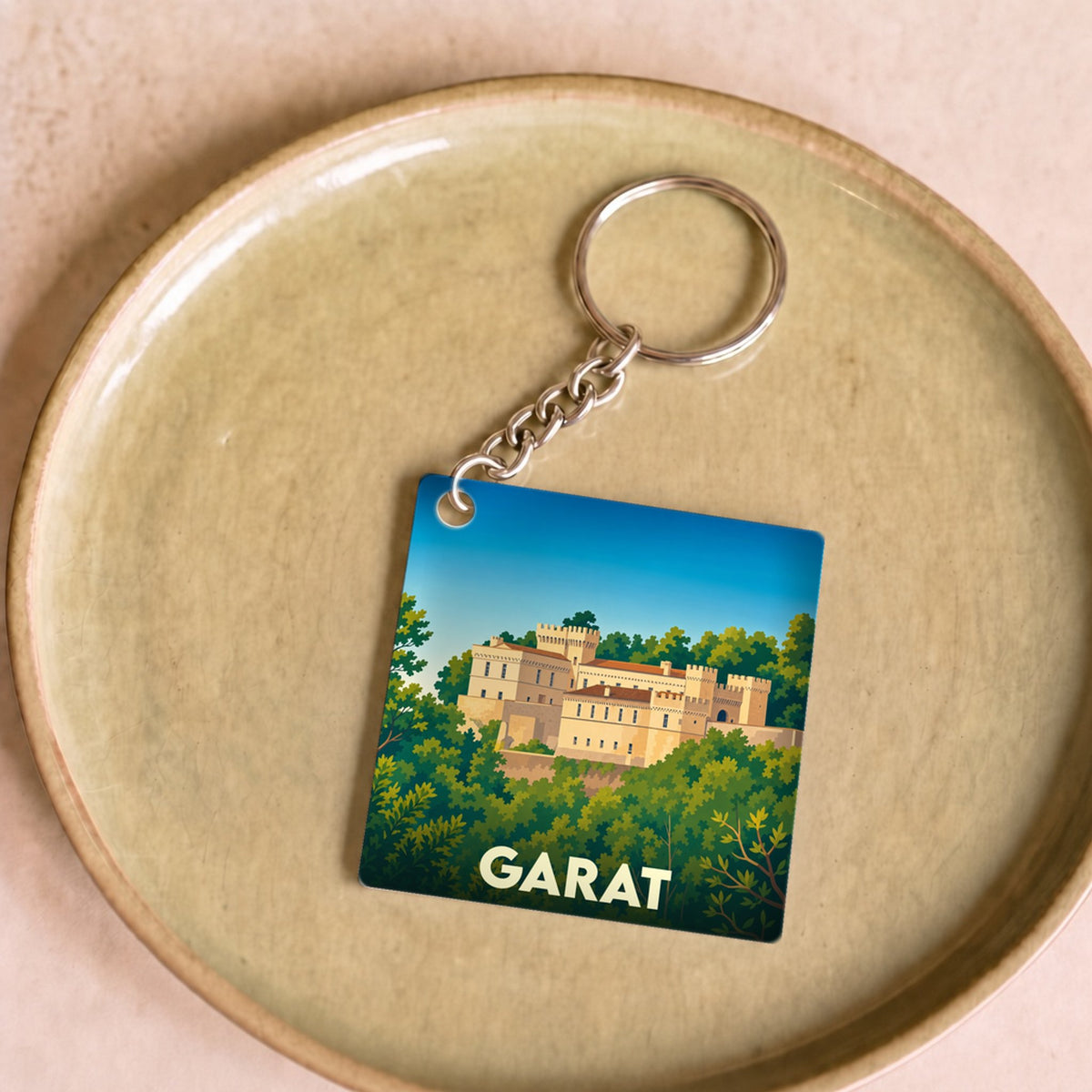 Porte-clés souvenir de la ville de Garat illustré d'un château entouré de verdure sous un ciel bleu.