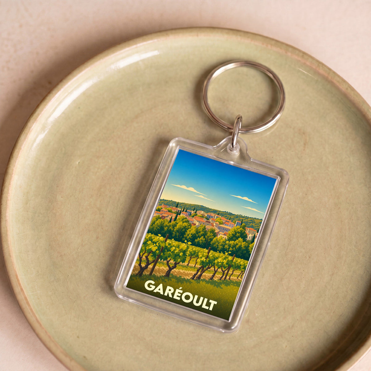 Porte-clés souvenir de la ville de Garéoult illustré d'un paysage de vignobles provençaux.