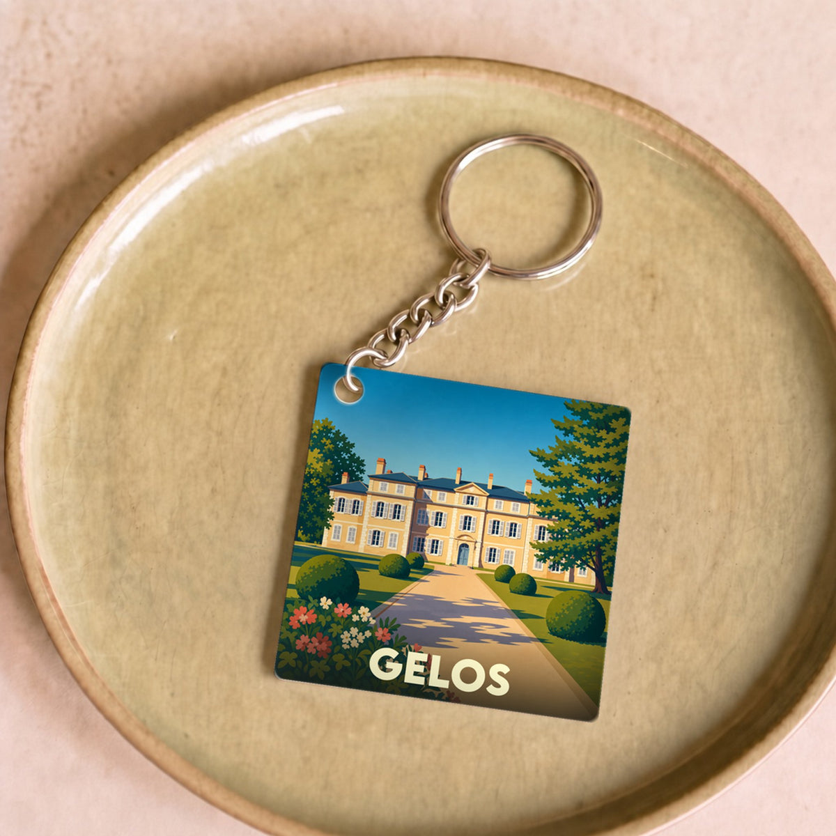 Porte-clés souvenir de la ville de Gelos avec une illustration stylisée d'un domaine historique.