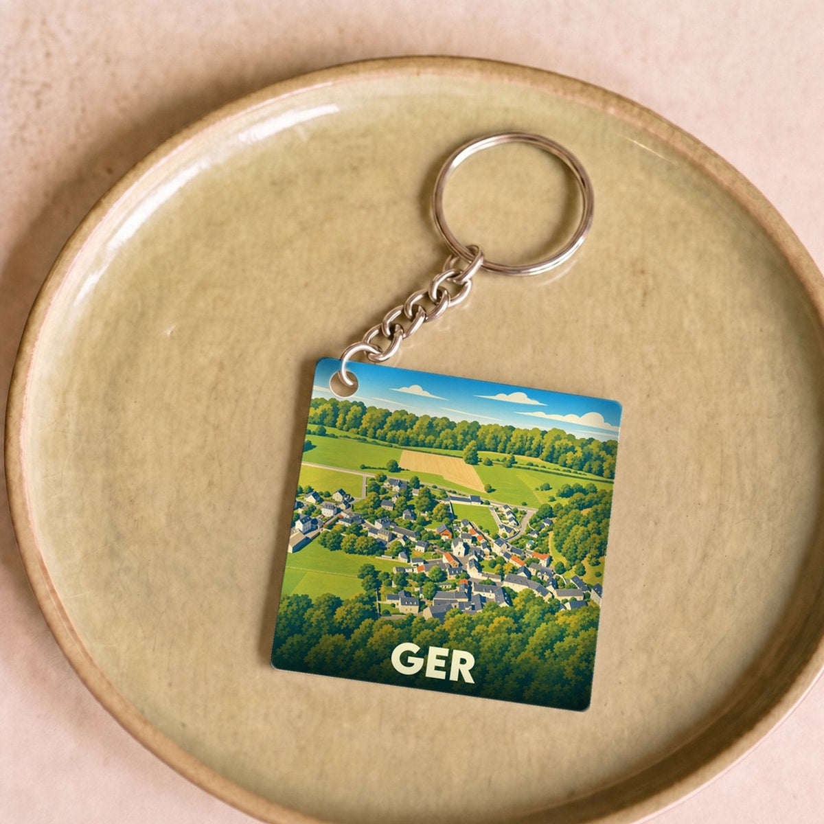 Porte-clés souvenir de la ville de Ger avec une illustration stylisée d'un paysage rural.