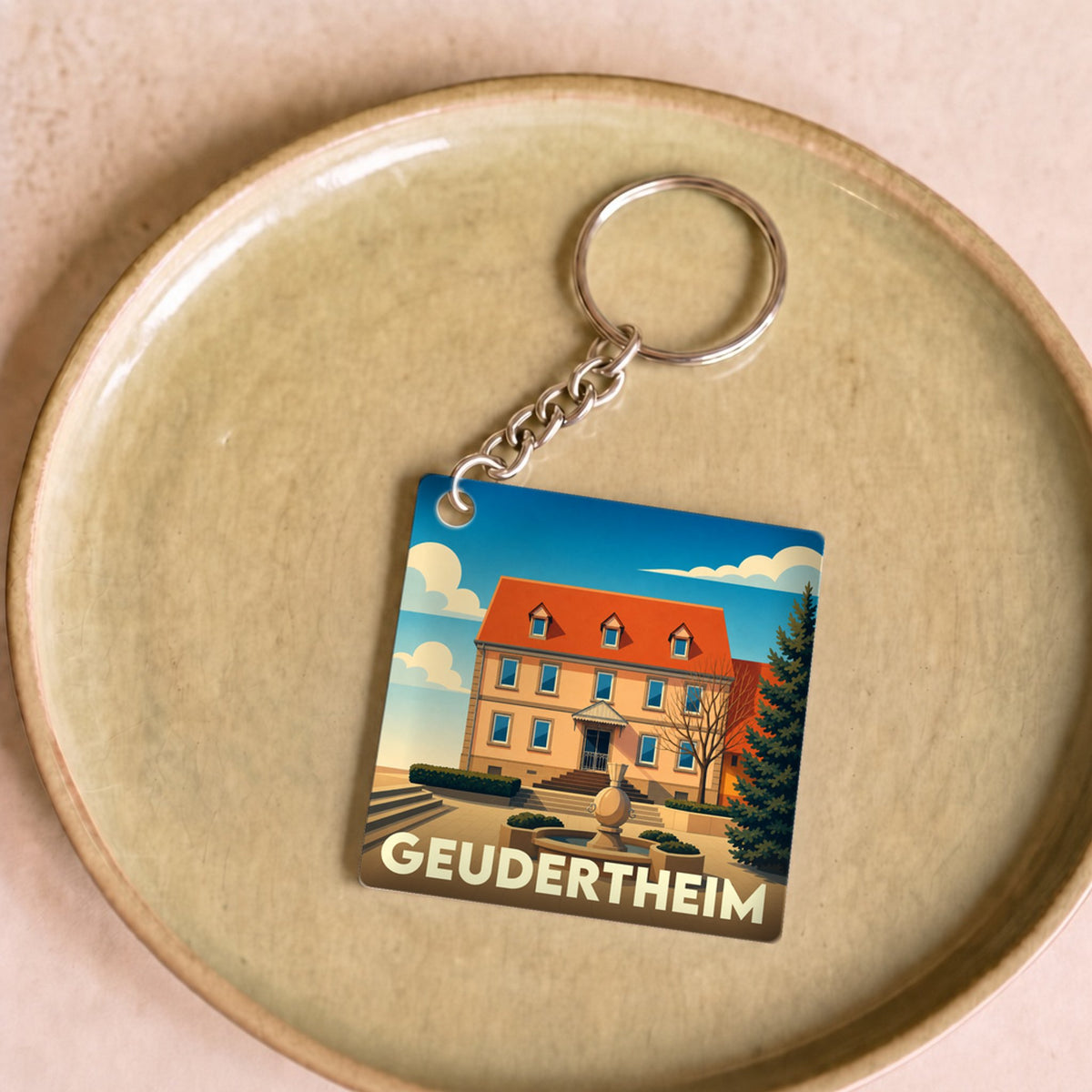 Porte-clés souvenir de la ville de Geudertheim avec une illustration stylisée d'un bâtiment historique et sa fontaine.