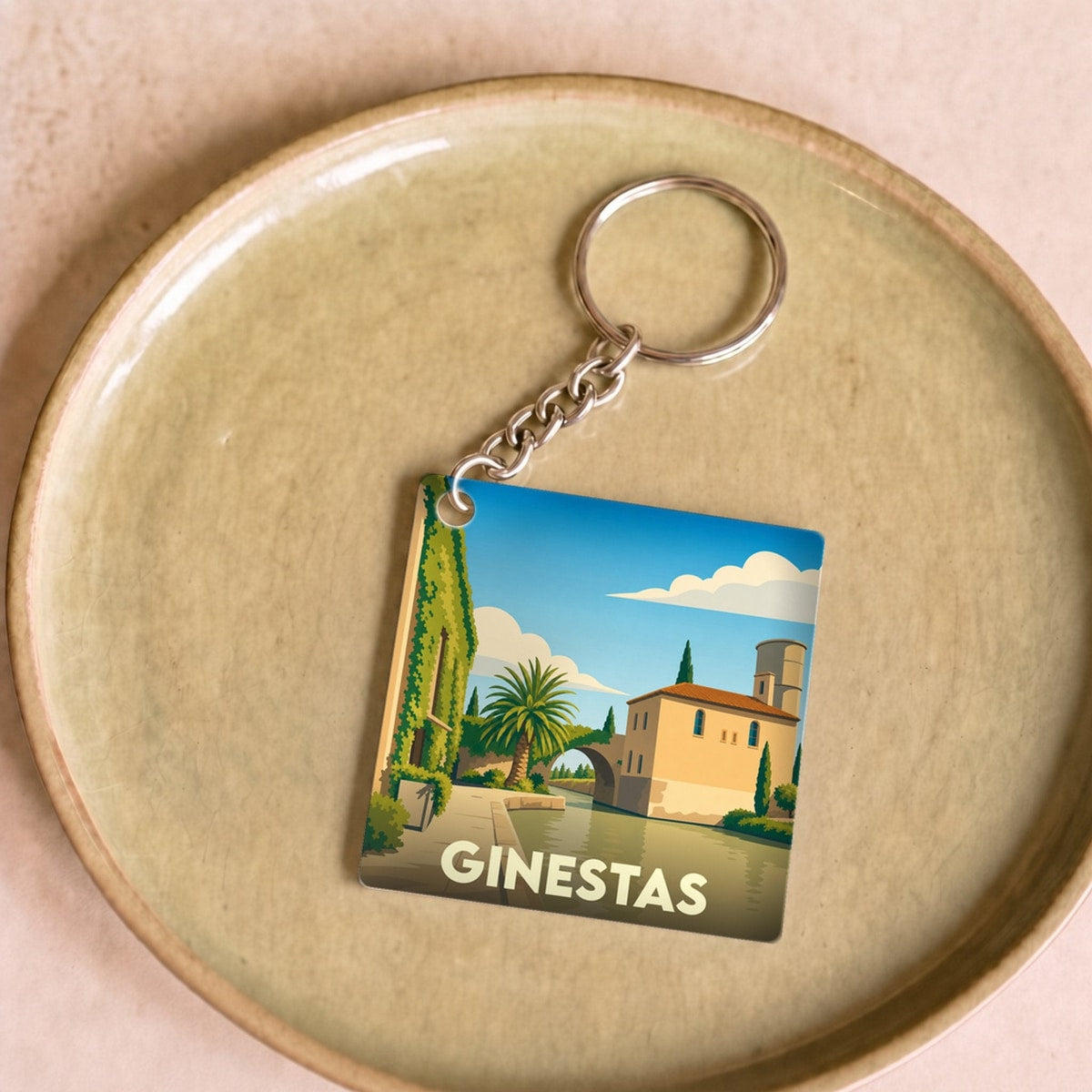 Porte-clés souvenir de la ville de Ginestas avec une illustration stylisée d'un paysage méditerranéen.