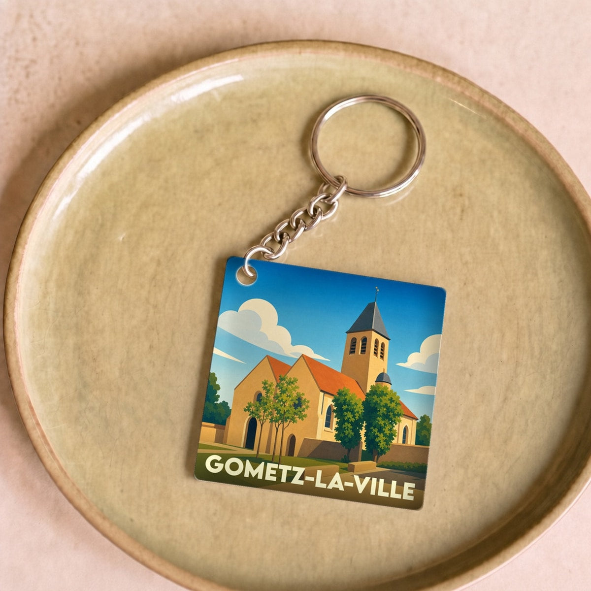Porte-clés souvenir de Gometz-la-Ville avec une illustration stylisée de son église sous un ciel bleu.