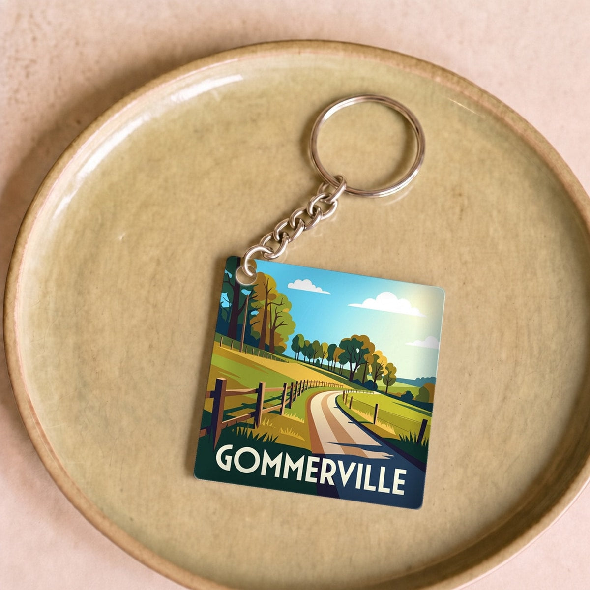 Porte-clés souvenir de la ville de Gommerville avec une illustration stylisée d'un paysage champêtre.