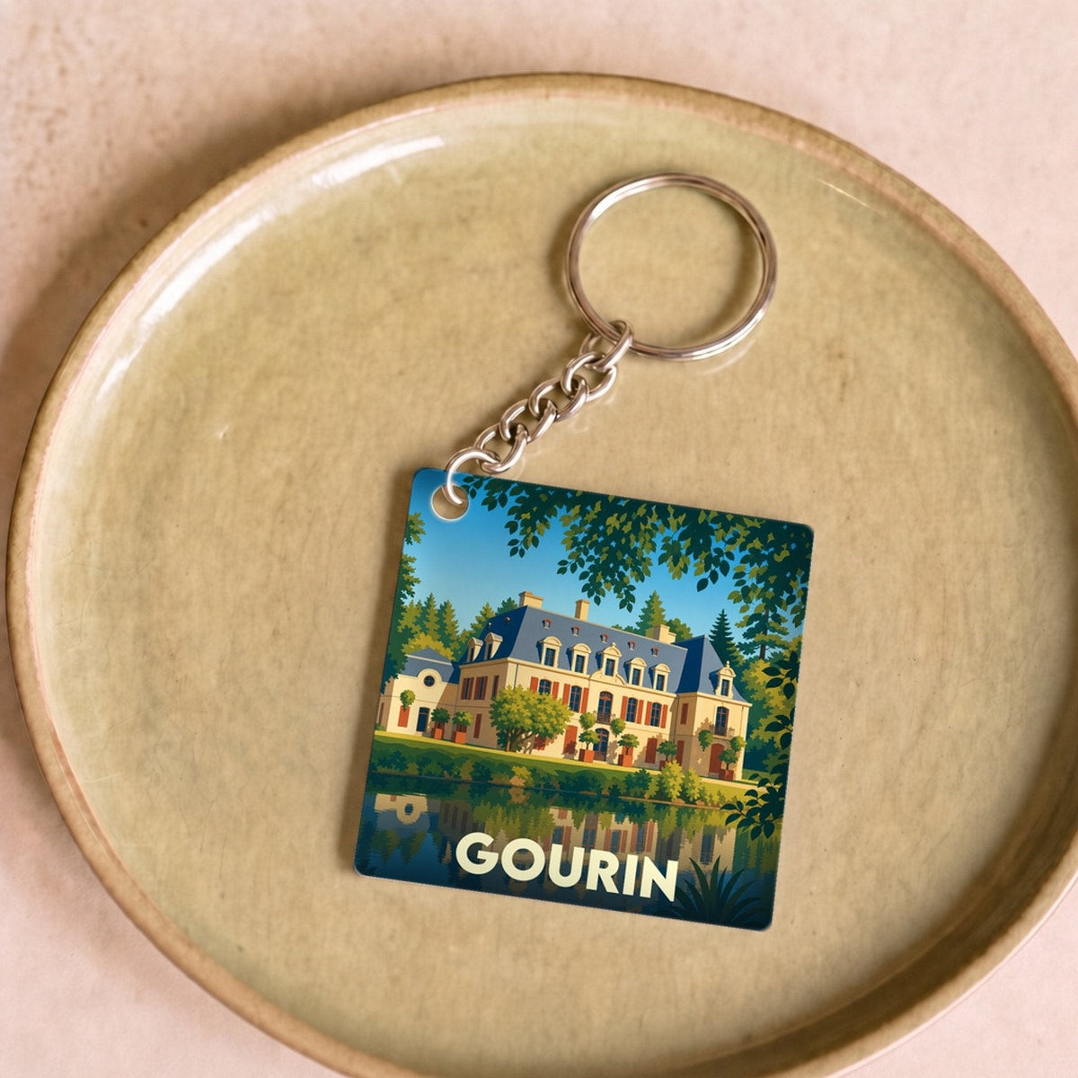 Porte-clés souvenir de la ville de Gourin avec une illustration stylisée d'un manoir se reflétant dans l'eau.