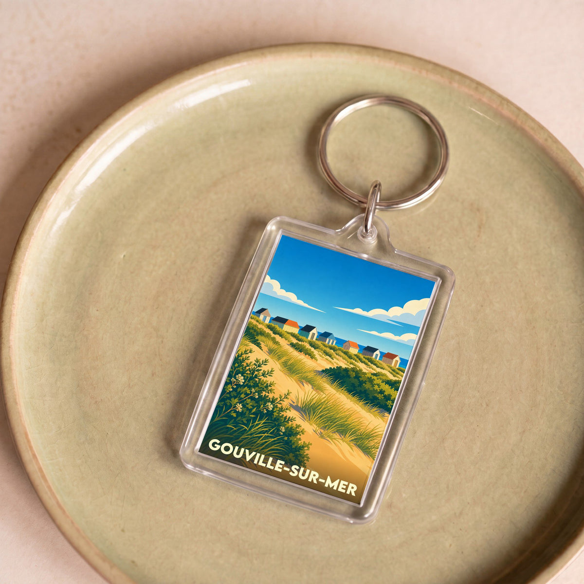 Porte-clés souvenir de la ville de Gouville-sur-Mer avec une illustration stylisée des cabines de plage et des dunes.