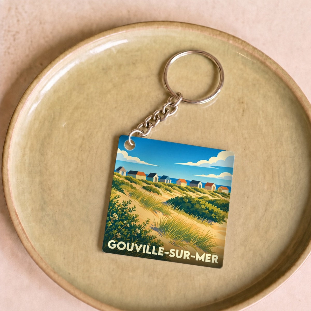 Porte-clés souvenir de la ville de Gouville-sur-Mer avec une illustration stylisée des cabines de plage et des dunes.