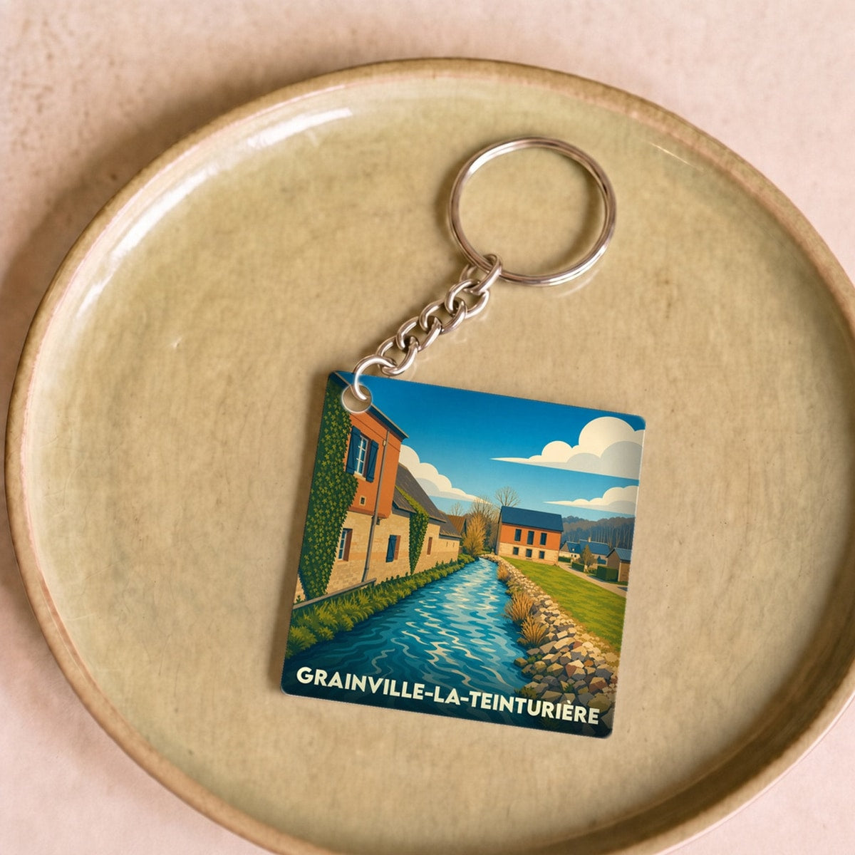 Porte-clés souvenir de Grainville-la-Teinturière avec une illustration stylisée de la rivière traversant le village.