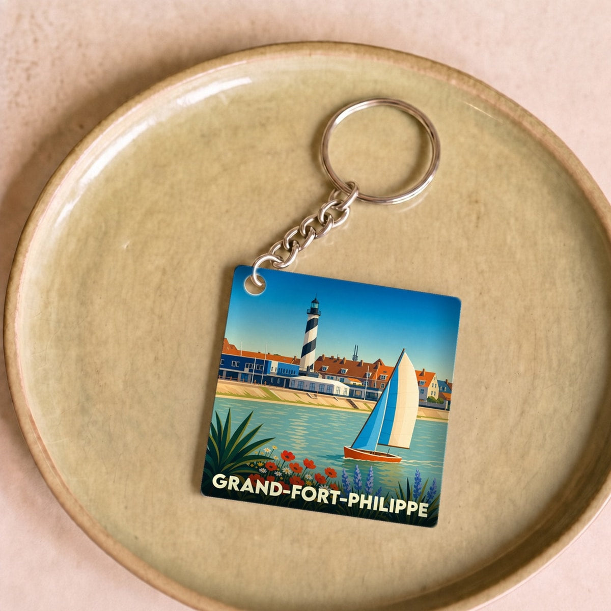 Porte-clés souvenir de Grand-Fort-Philippe avec une illustration stylisée de son phare et d'un voilier.
