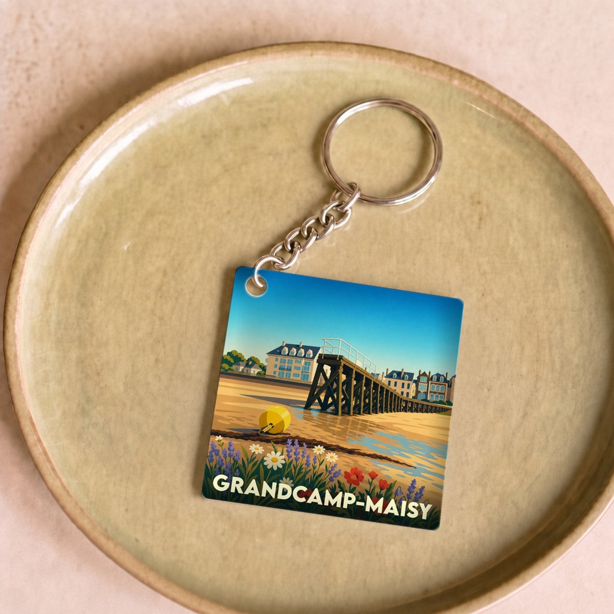 Porte-clés souvenir de la ville de Grandcamp-Maisy avec une illustration stylisée d'un paysage côtier.