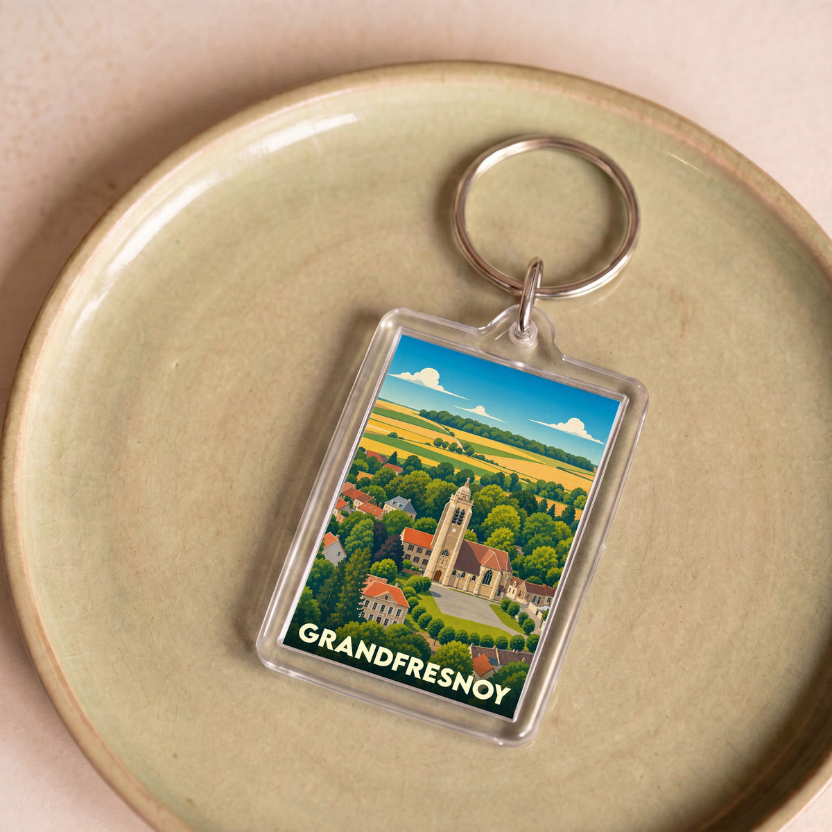 Porte-clés souvenir de la ville de Grandfresnoy avec une illustration stylisée de son église et de ses paysages.