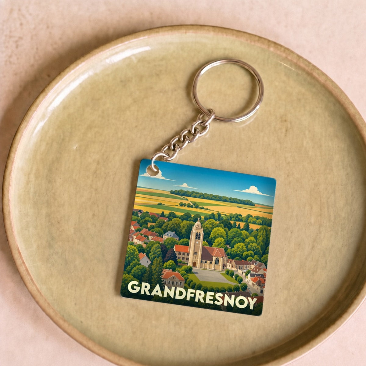 Porte-clés souvenir de la ville de Grandfresnoy avec une illustration stylisée de son église et de ses paysages.