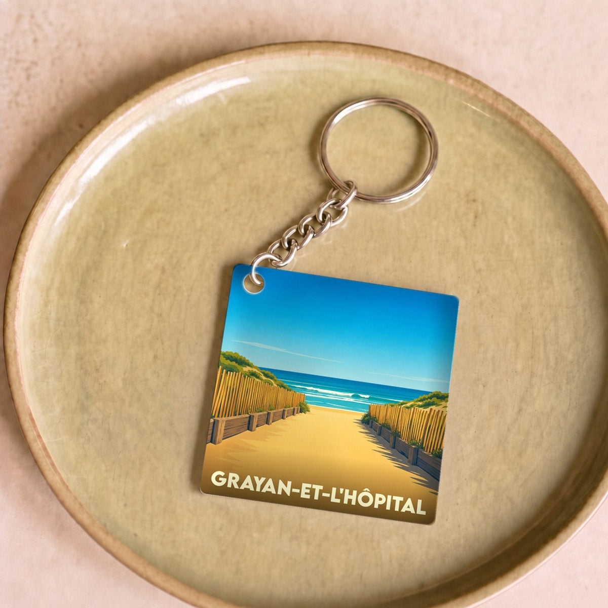 Porte-clés souvenir de la ville de Grayan-et-l'Hôpital avec une illustration stylisée d'un accès à la plage.