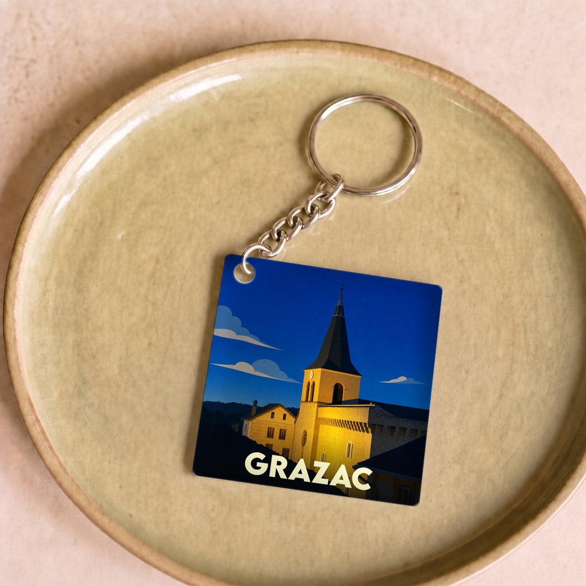 Porte-clés souvenir de la ville de Grazac avec une illustration stylisée de son église sous un ciel nocturne.