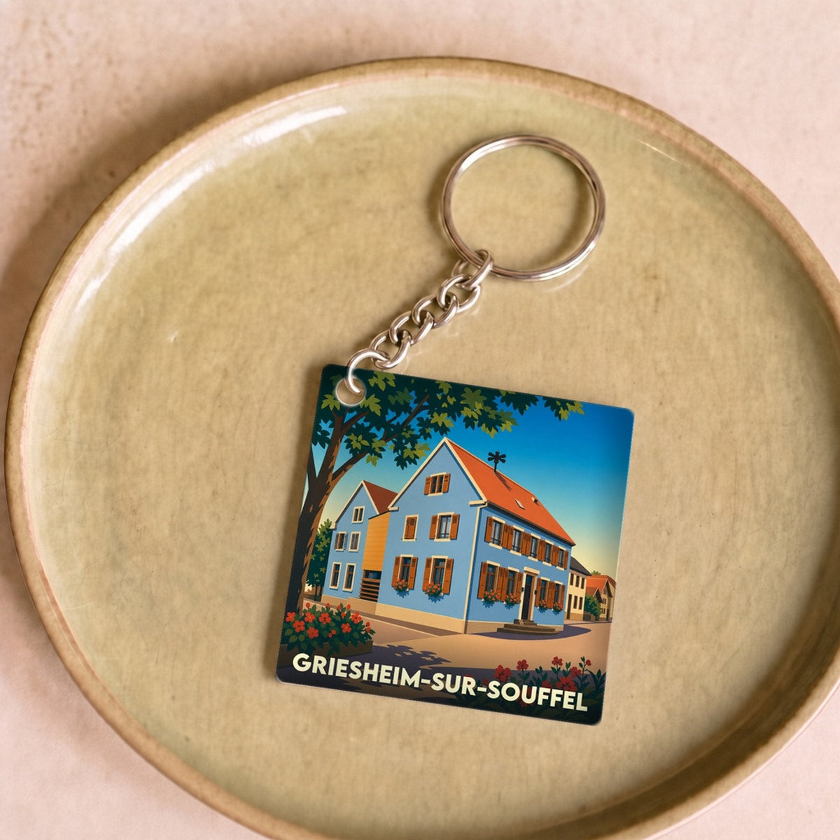 Porte-clés souvenir de la ville de Griesheim-sur-Souffel avec une illustration stylisée d'une maison alsacienne bleue.