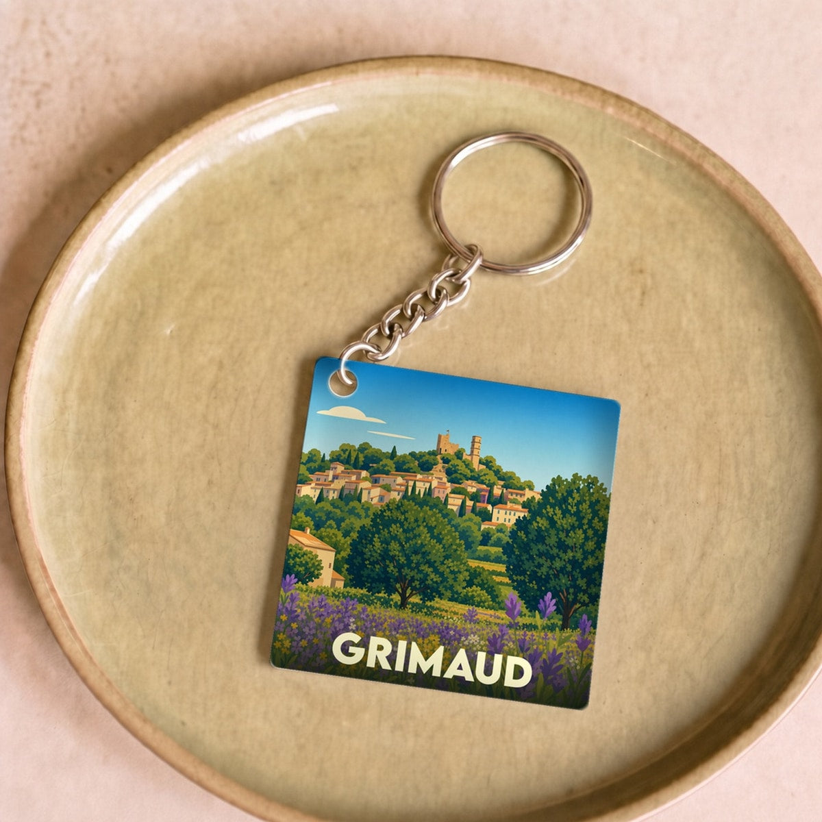Porte-clés souvenir de la ville de Grimaud avec une illustration stylisée d'un paysage provençal.