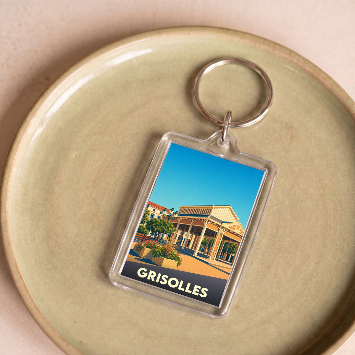 Porte-clés souvenir de la ville de Grisolles avec une illustration stylisée de sa halle couverte.