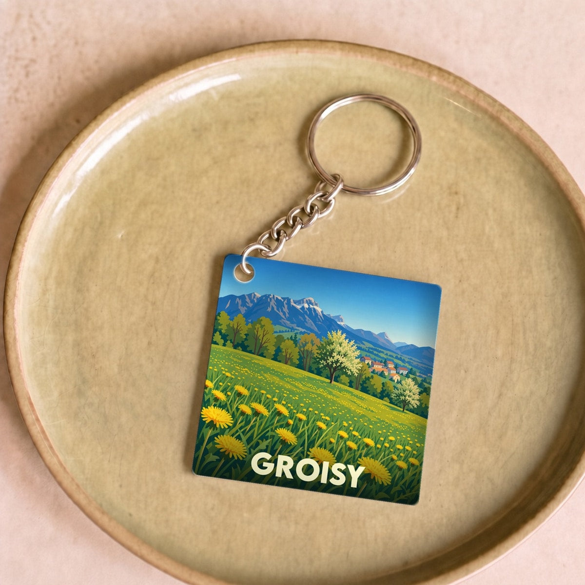 Porte-clés souvenir de la ville de Groisy avec une illustration stylisée d'un paysage montagneux fleuri.