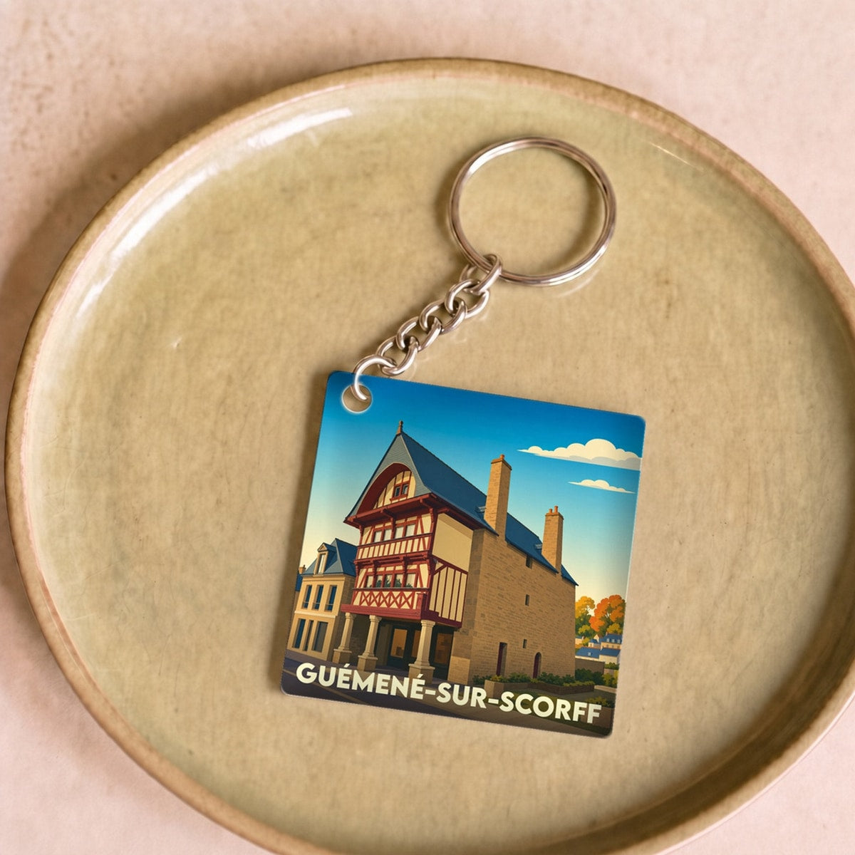 Porte-clés souvenir de la ville de Guémené-sur-Scorff avec une illustration stylisée d'une maison traditionnelle à colombages.