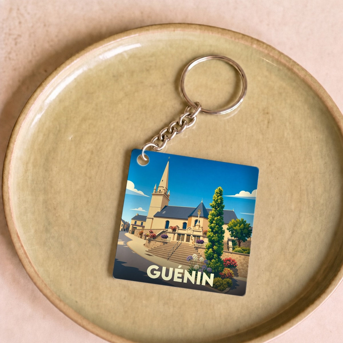 Porte-clés souvenir de la ville de Guénin avec une illustration stylisée de son église.