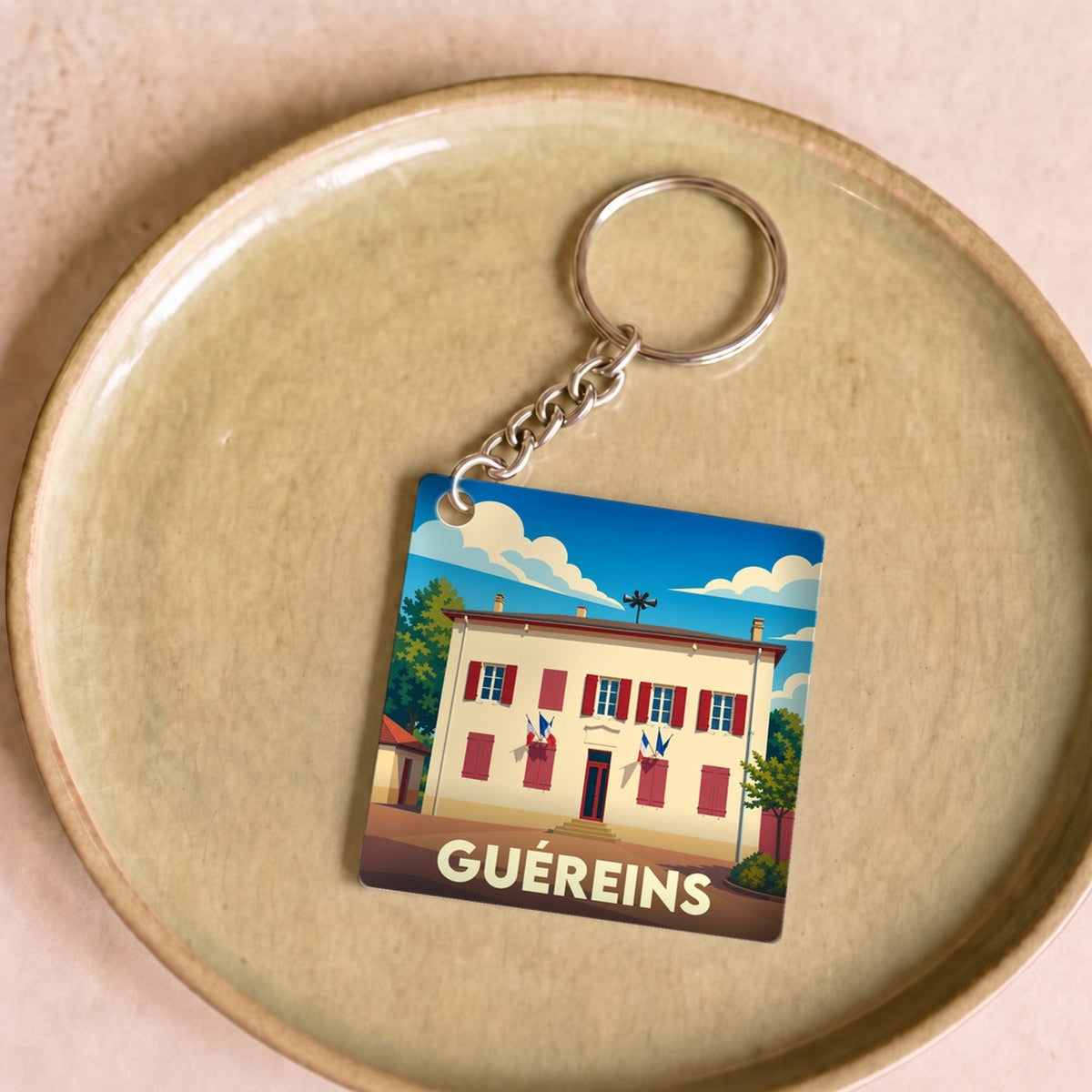 Porte-clés souvenir de la ville de Guéreins avec une illustration stylisée de la mairie.