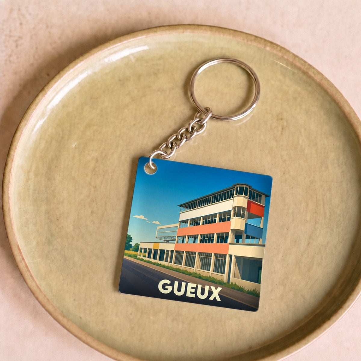 Porte-clés souvenir de la ville de Gueux avec une illustration stylisée de ses anciens stands de circuit.
