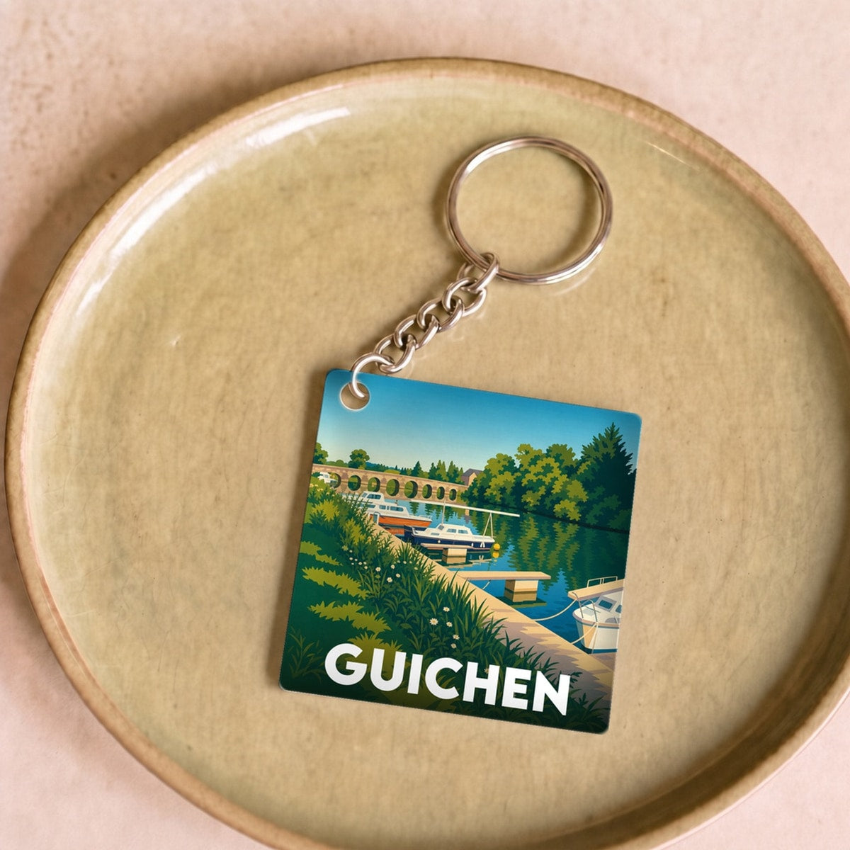 Porte-clés souvenir de la ville de Guichen avec une illustration stylisée d'un paysage fluvial.
