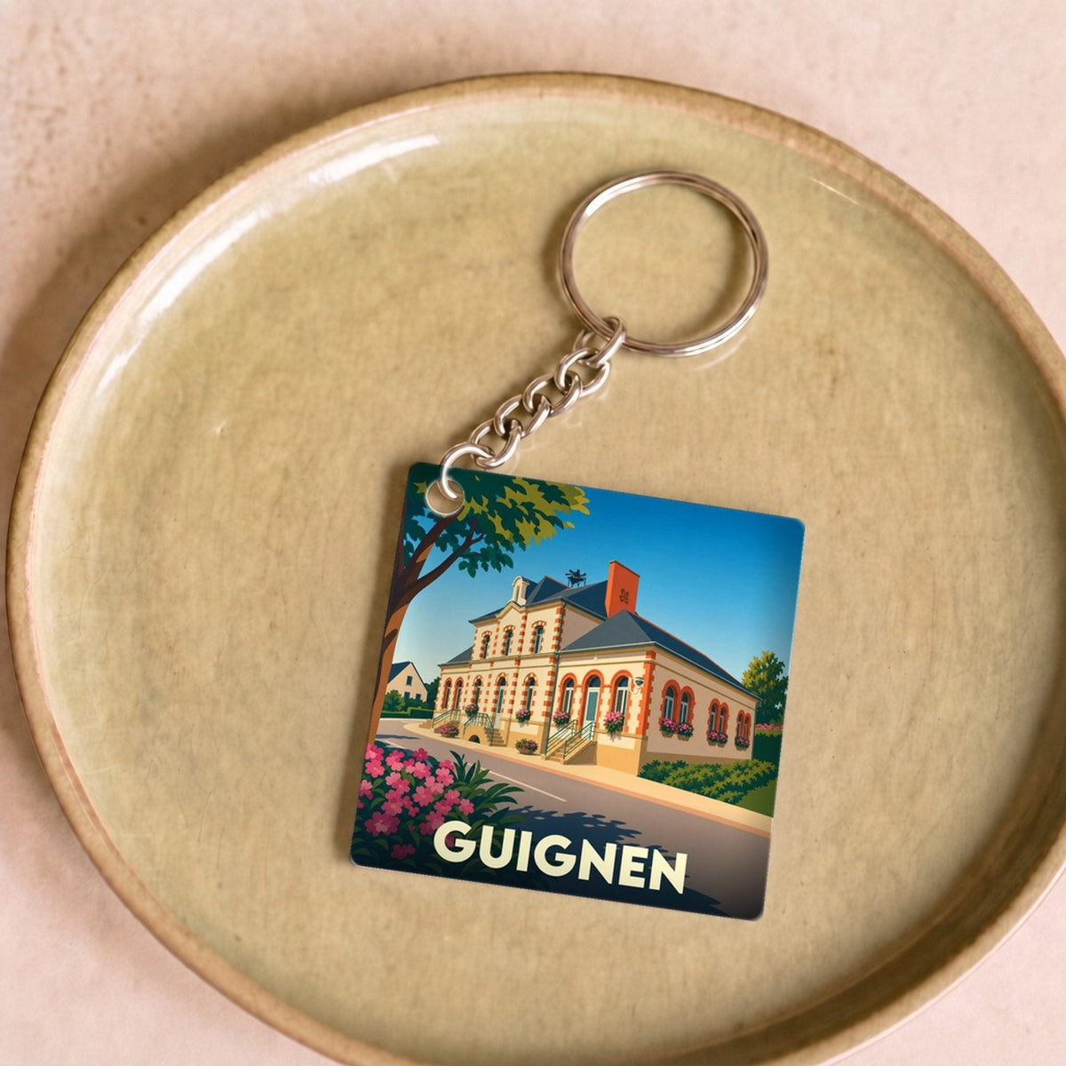 Porte-clés souvenir de la ville de Guignen avec une illustration stylisée de sa mairie.