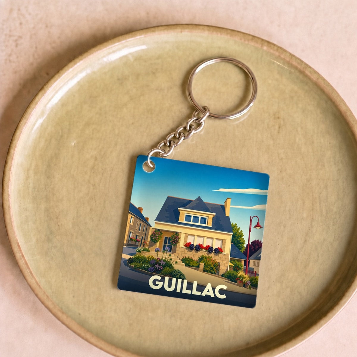 Porte-clés souvenir de la ville de Guillac avec une illustration stylisée d'une maison fleurie.