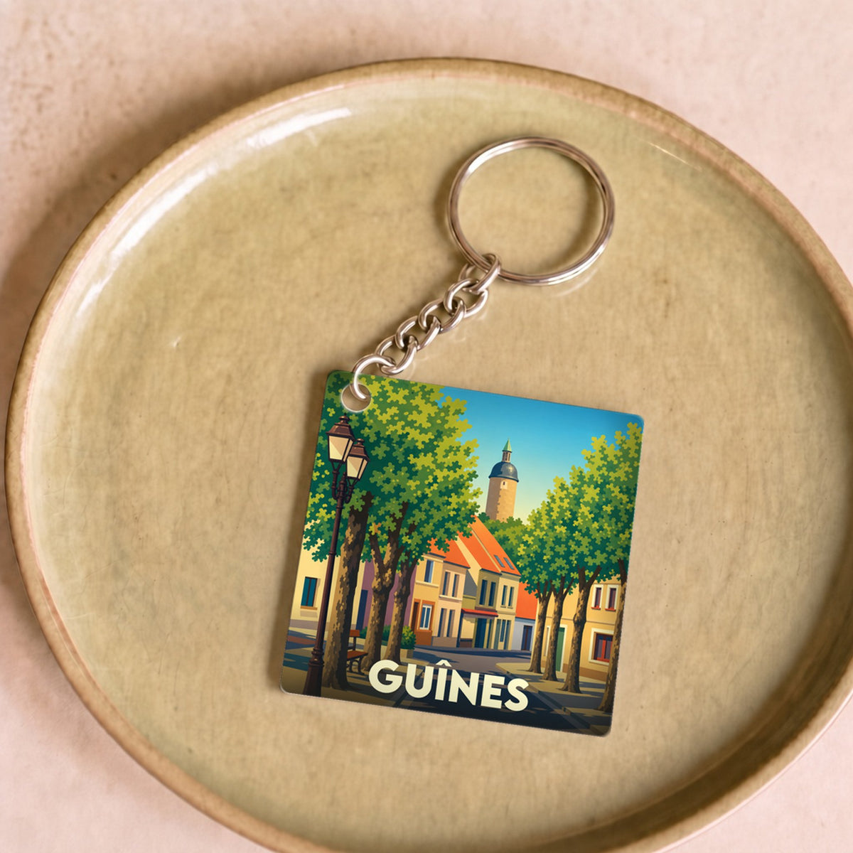Porte-clés souvenir de la ville de Guînes avec une illustration stylisée.