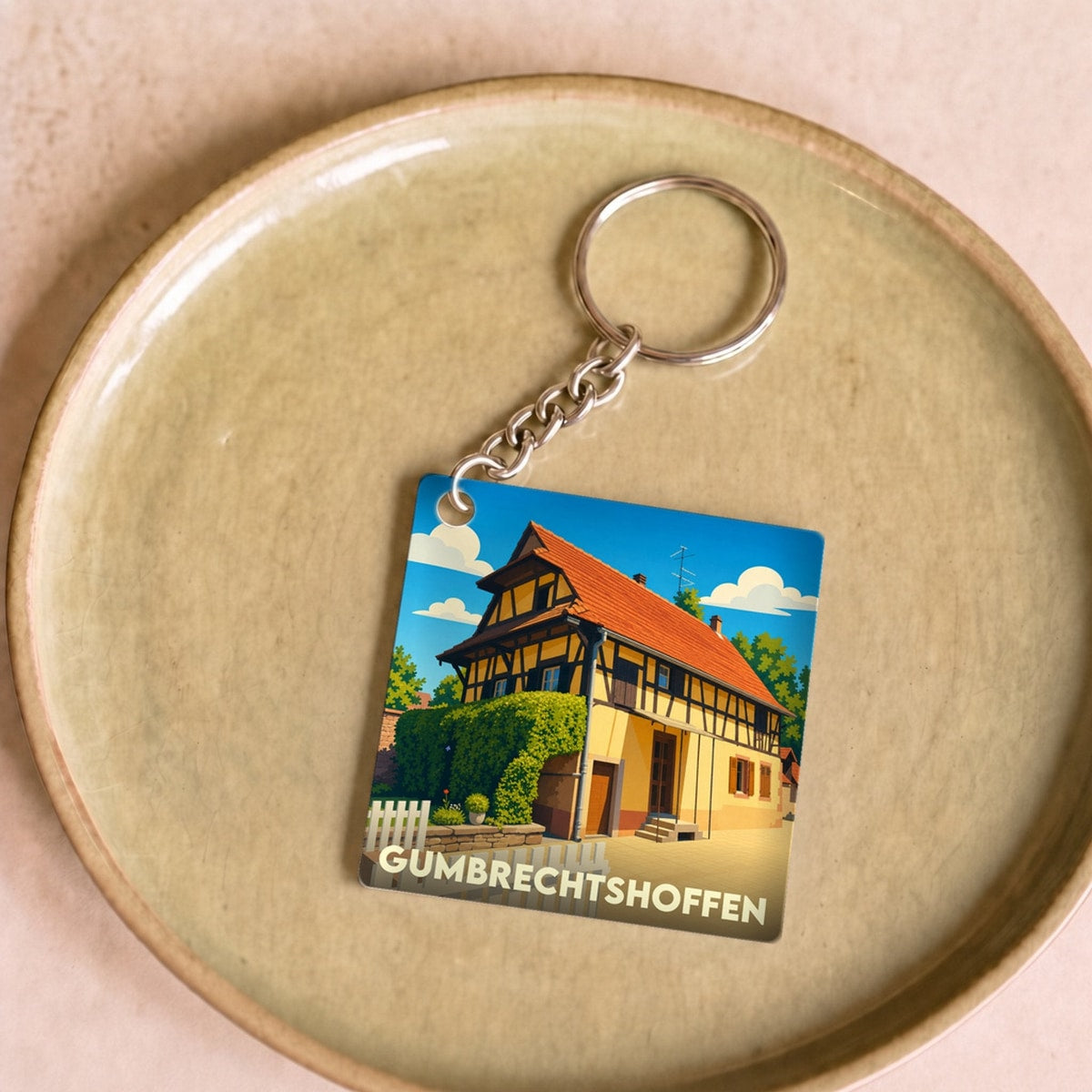 Porte-clés souvenir de la ville de Gumbrechtshoffen avec une illustration stylisée d'une maison traditionnelle à colombages.