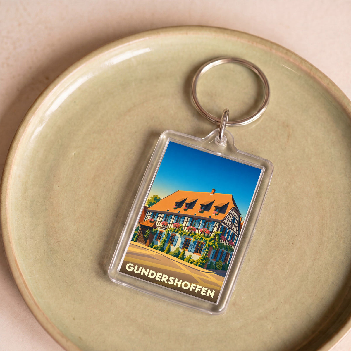 Porte-clés souvenir de la ville de Gundershoffen avec une illustration stylisée d'une maison alsacienne.