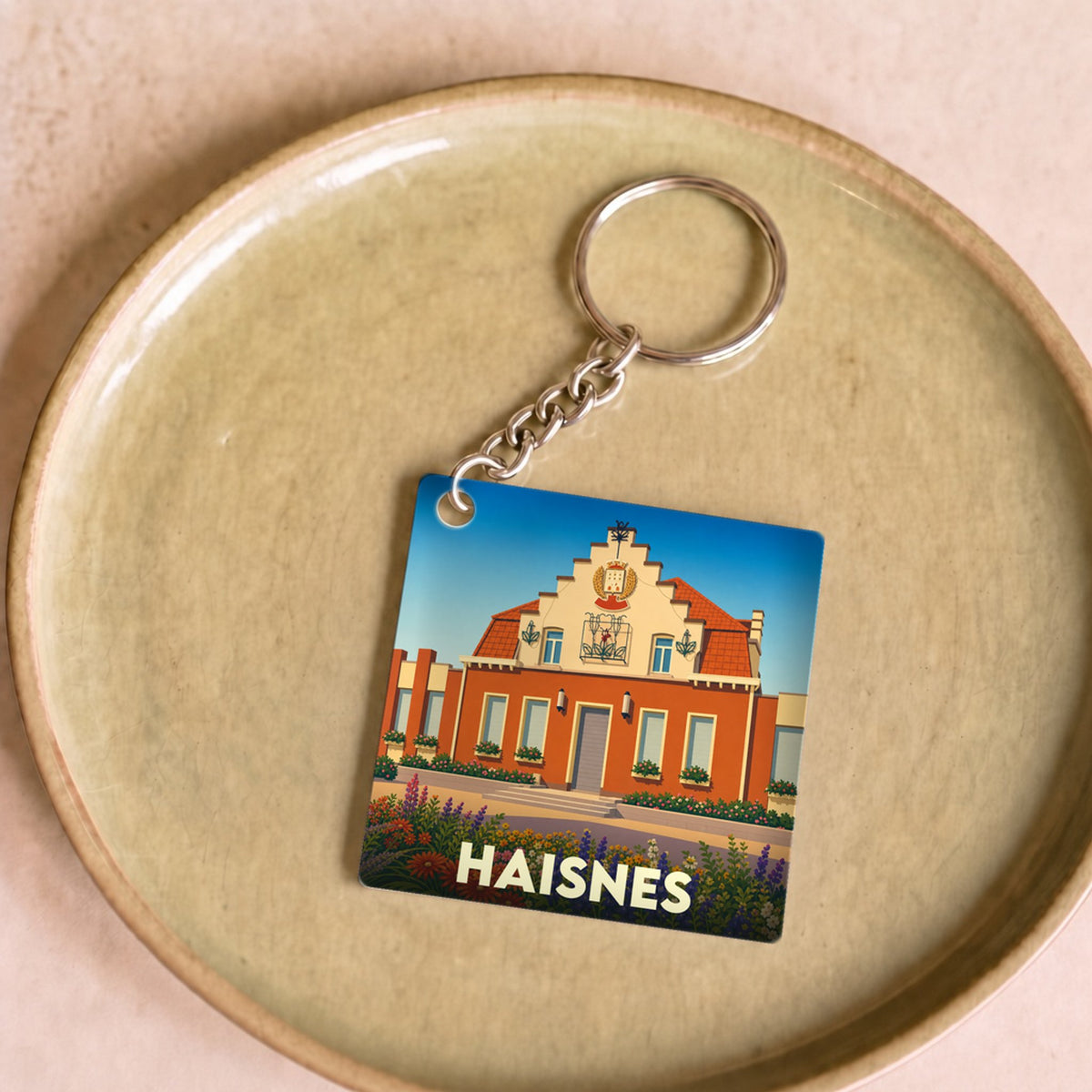 Porte-clés souvenir de la ville de Haisnes avec une illustration stylisée de son hôtel de ville fleuri.