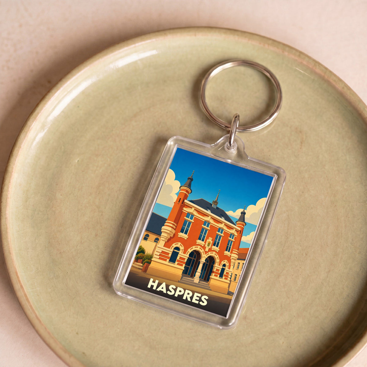 Porte-clés souvenir de la ville de Haspres avec une illustration stylisée de son hôtel de ville.