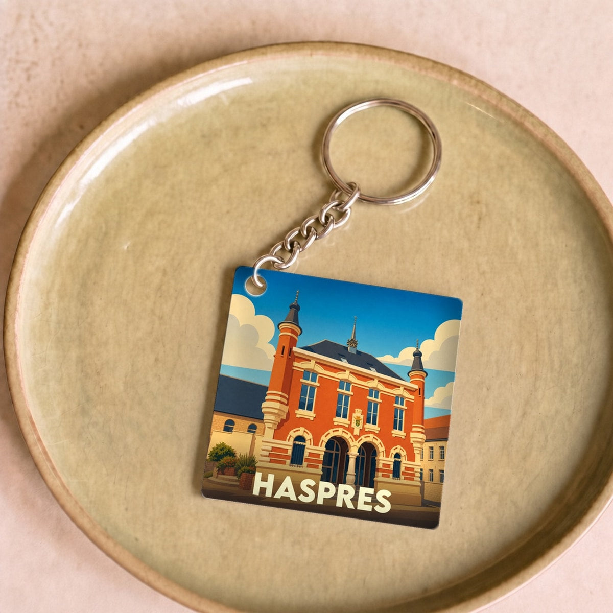 Porte-clés souvenir de la ville de Haspres avec une illustration stylisée de son hôtel de ville.