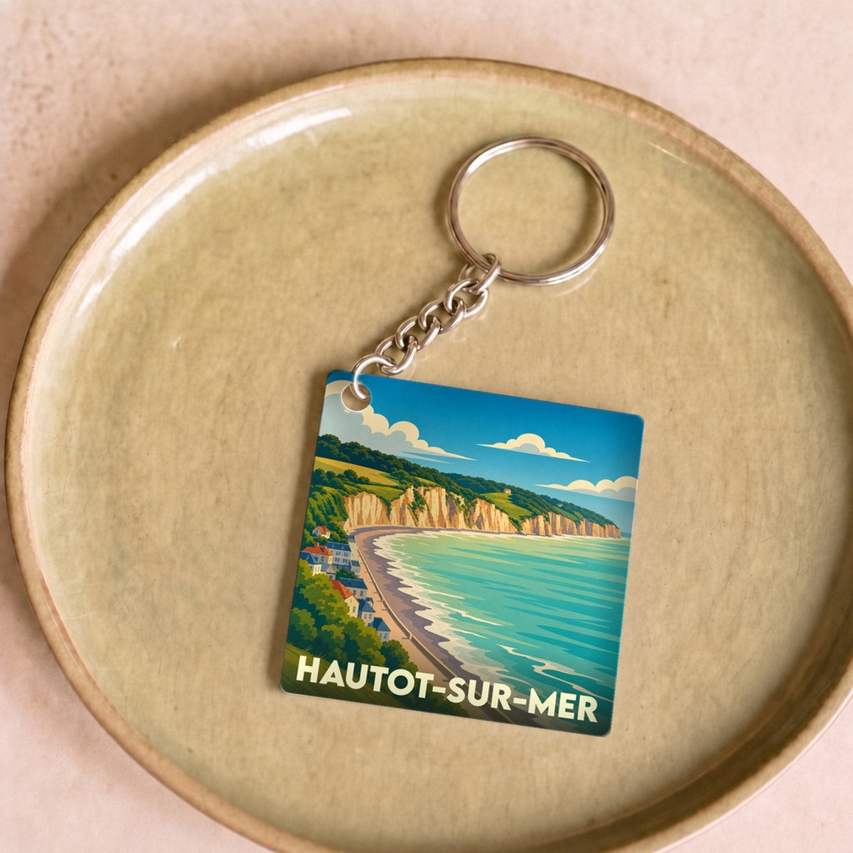Porte-clés souvenir de la ville de Hautot-sur-Mer avec une illustration stylisée de ses falaises et de sa plage.