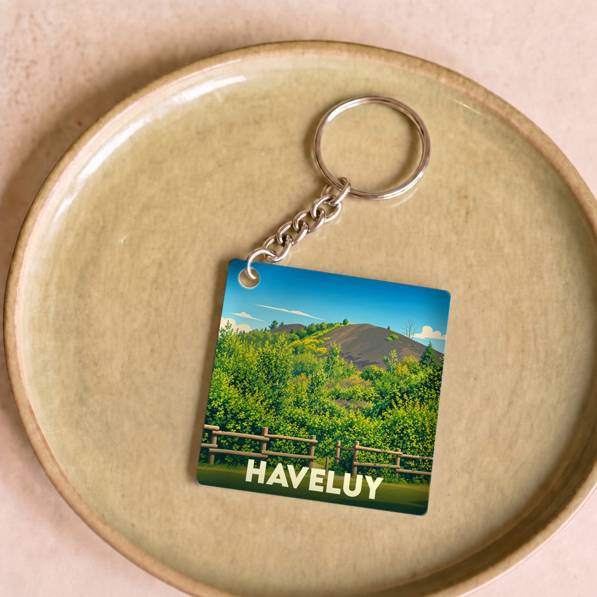 Porte-clés souvenir de la ville de Haveluy avec une illustration stylisée de paysage naturel.