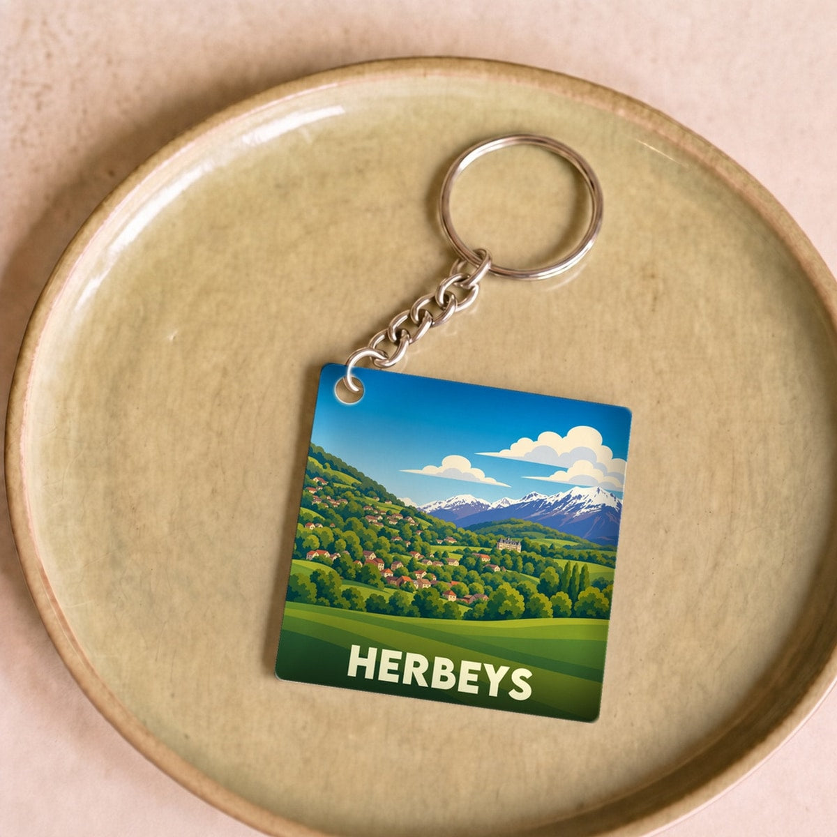 Porte-clés souvenir de la ville de Herbeys avec une illustration de paysage de montagne stylisée.
