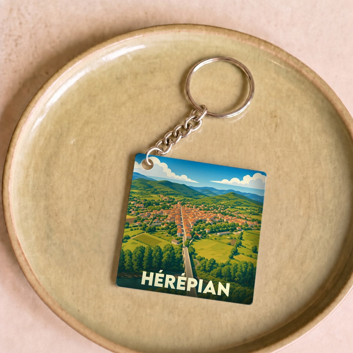 Porte-clés souvenir de la ville de Hérépian avec une illustration stylisée de son paysage.