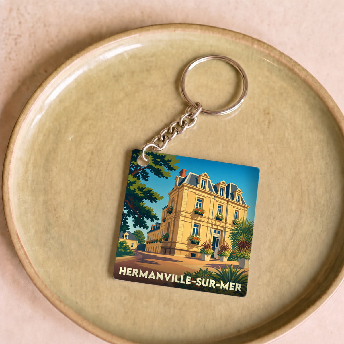 Porte-clés souvenir de la ville de Hermanville-sur-Mer avec une illustration stylisée d'une villa balnéaire.