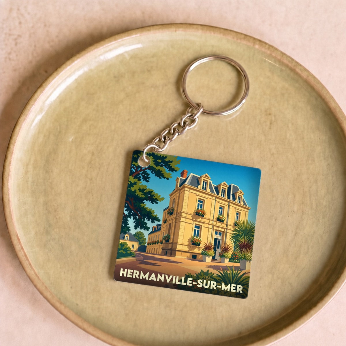 Porte-clés souvenir de la ville de Hermanville-sur-Mer avec une illustration stylisée d'une villa balnéaire.