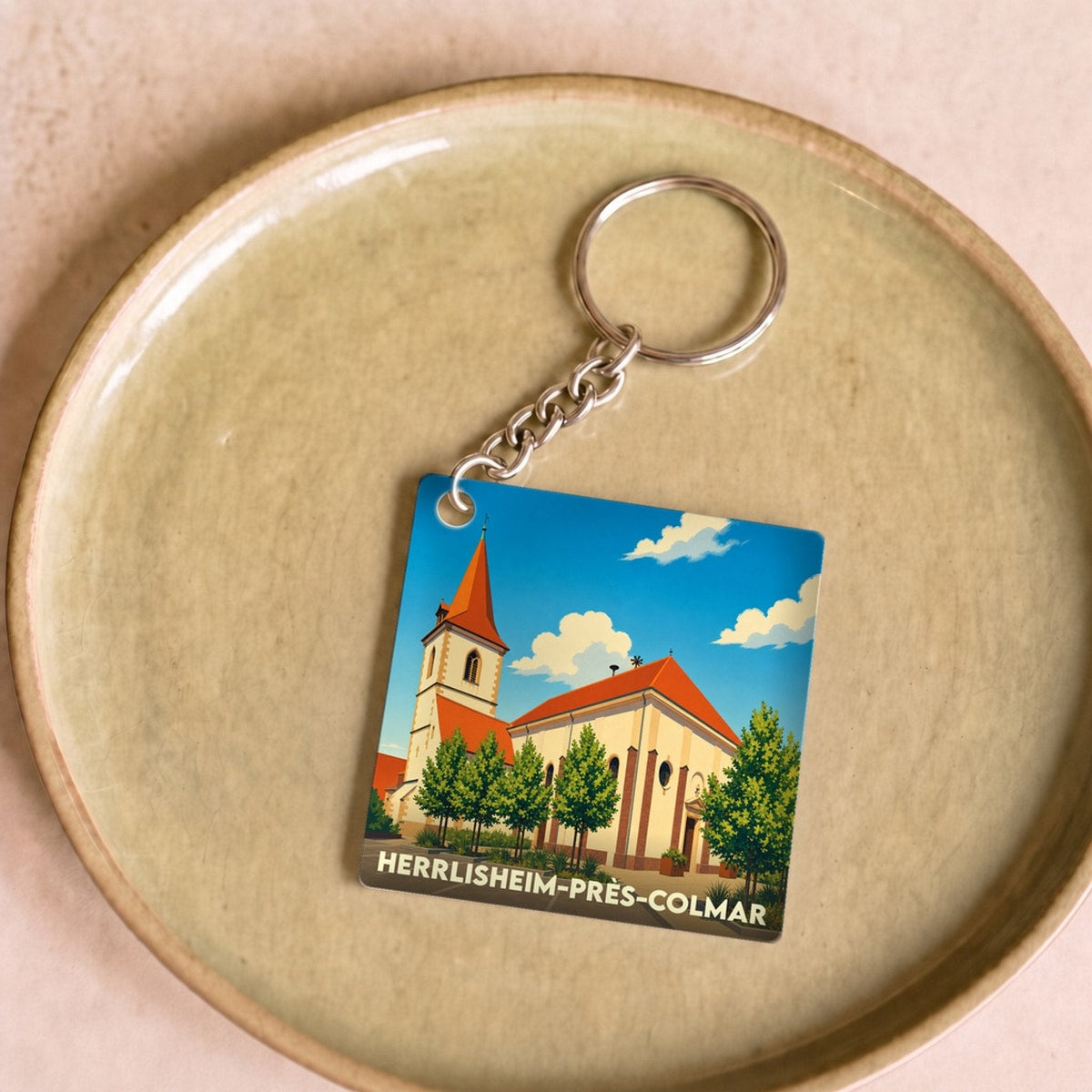 Porte-clés souvenir de la ville de Herrlisheim-près-Colmar avec une illustration stylisée de son église.