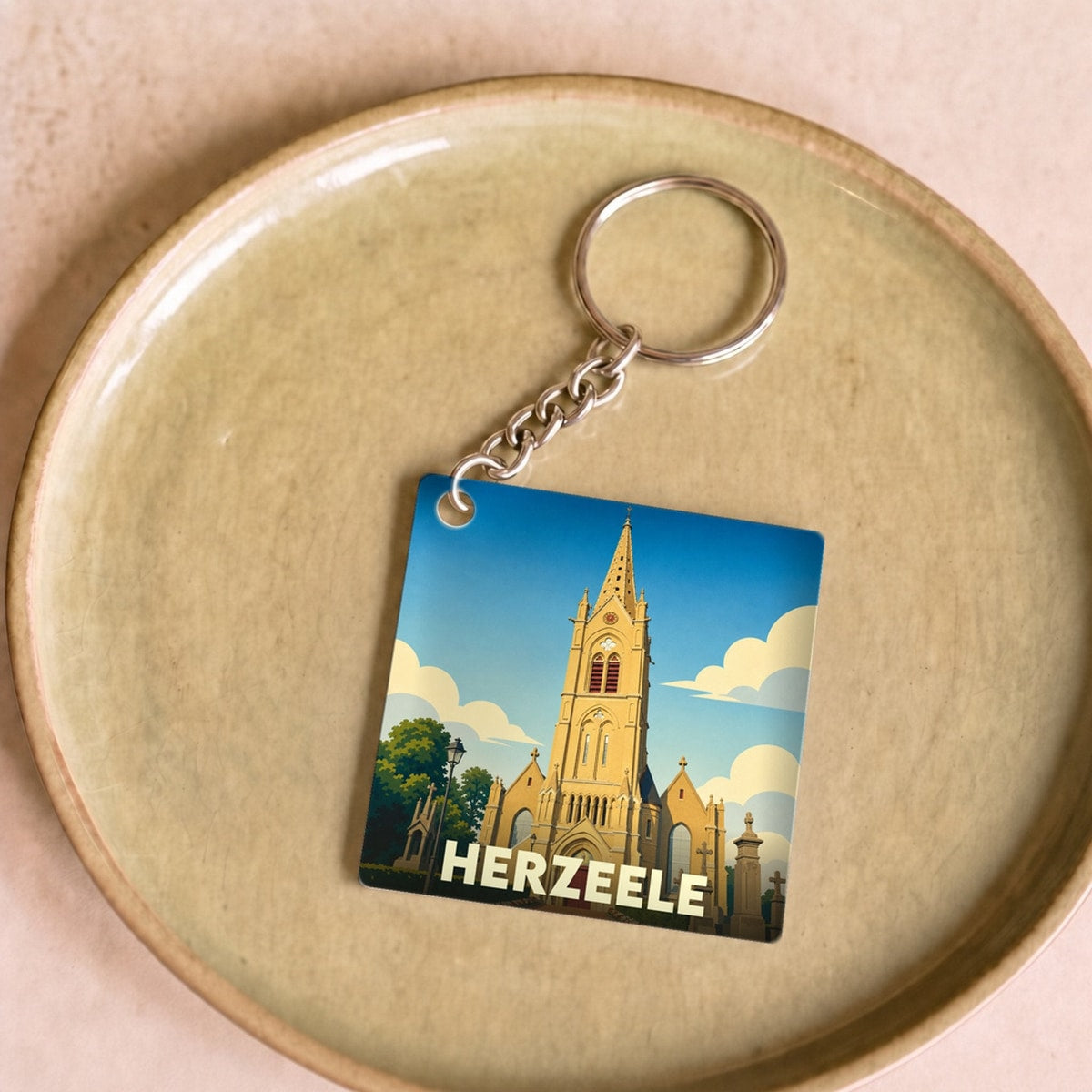Porte-clés souvenir de la ville de Herzeele avec une illustration stylisée de son église.