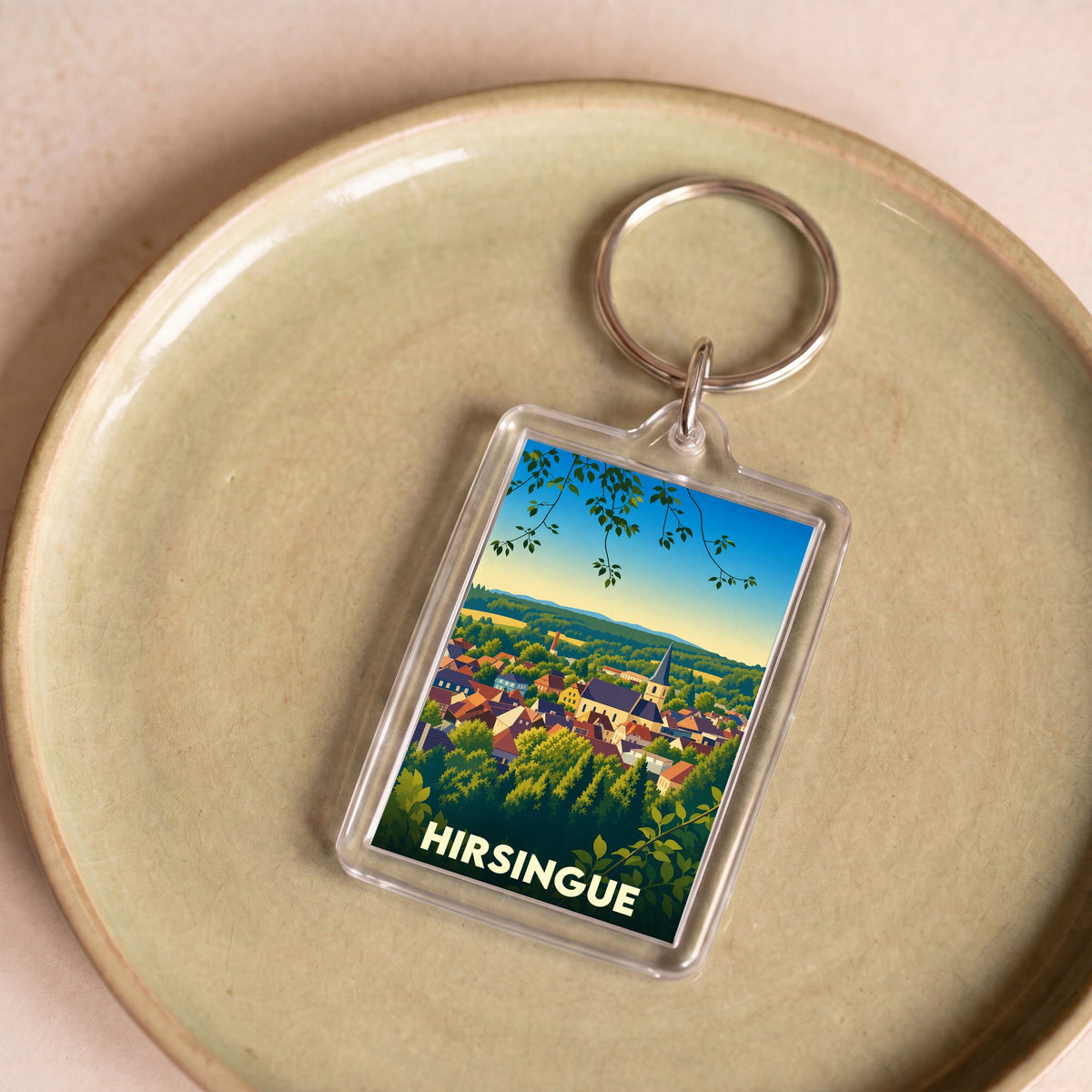Porte-clés souvenir de la ville de Hirsingue avec une illustration stylisée de son paysage.