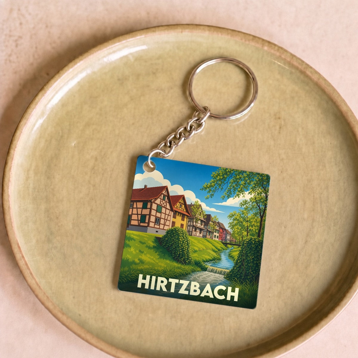 Porte-clés souvenir de la ville de Hirtzbach avec une illustration stylisée de maisons à colombages au bord de l'eau.